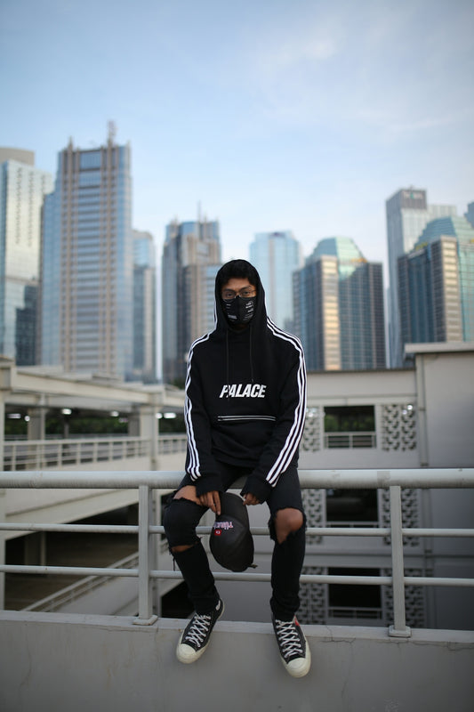 a man wearing a mask and sitting on a ledge with a city skyline behind him