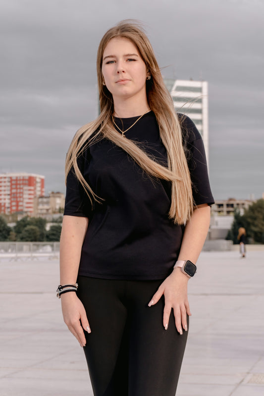 Young woman in black t-shirt and leggings standing outdoors