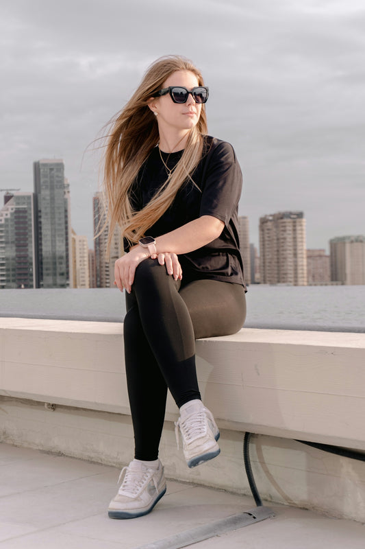 Woman in sunglasses sits on a ledge with cityscape background