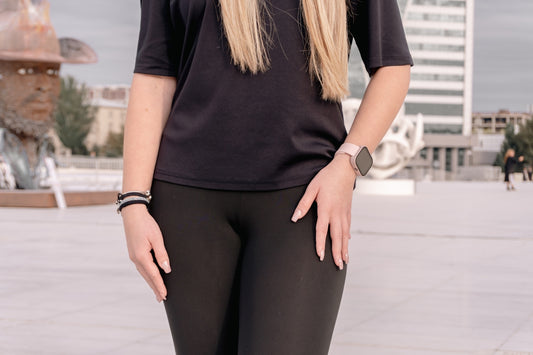 Woman in black outfit standing outdoors with sculpture.