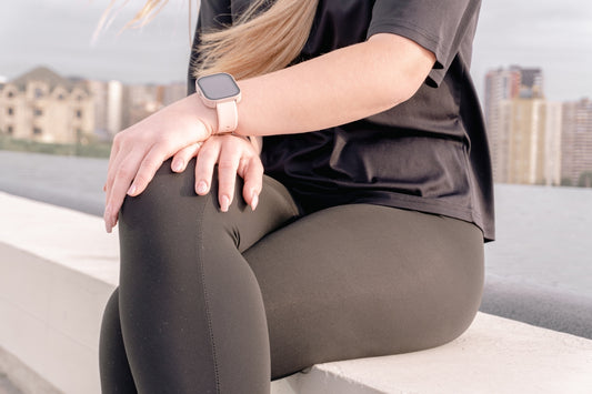 Woman in athletic wear sitting outdoors with city background.